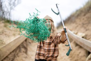A woman holding up a litter picker alongside the fishing nets they're made from